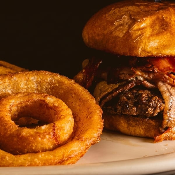 A juicy bacon cheeseburger with caramelized onions and a side of crispy onion rings.