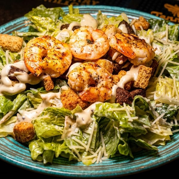Shrimp Caesar salad with grilled shrimp, croutons, parmesan cheese, and creamy dressing on a blue plate.