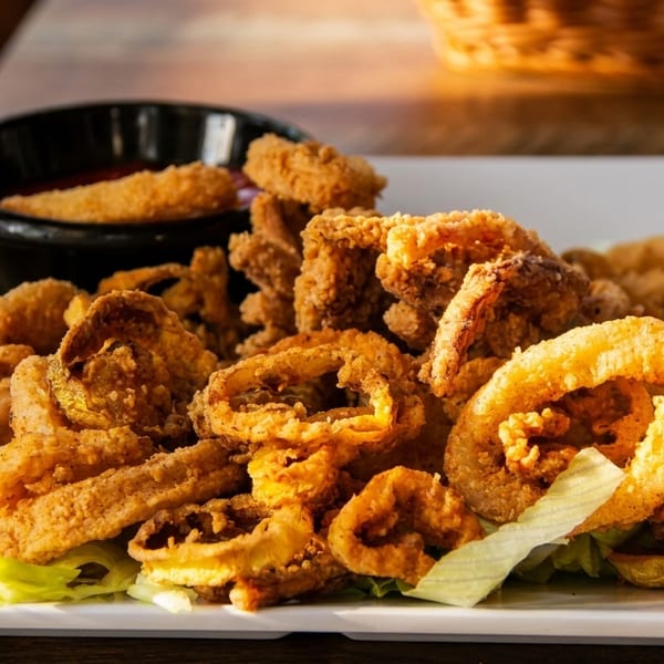 Crispy fried calamari and onion rings with a side of dipping sauce on a white plate.