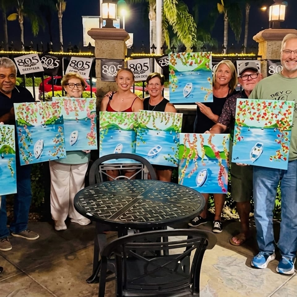 A group of people proudly display their boat and landscape paintings at an outdoor evening event.